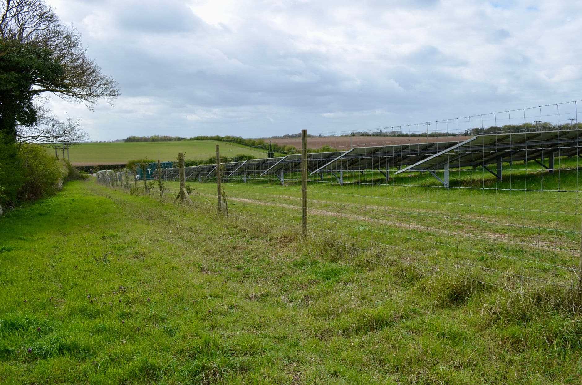 Solar panels installed across a rural field under a cloudy sky